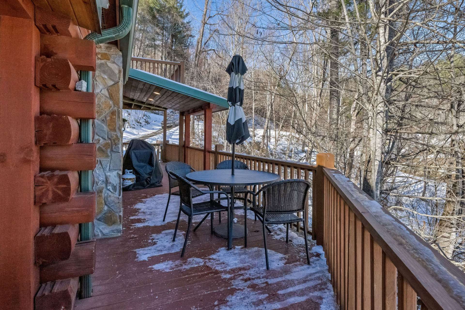 The upper deck wraps around three sides of the cabin, offering a seamless blend of covered and uncovered outdoor living spaces, perfect for enjoying the fresh mountain air in any weather.