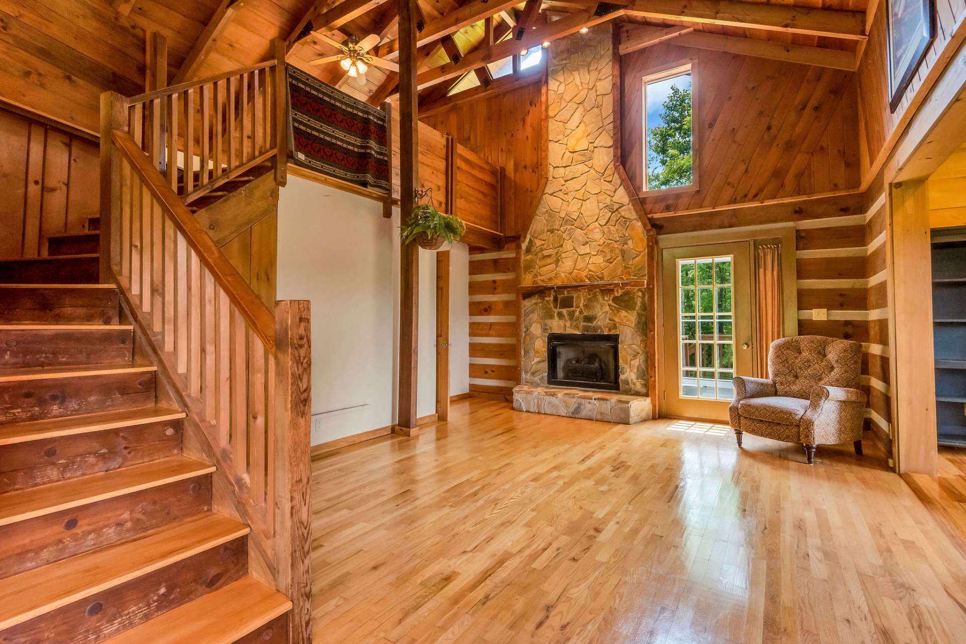 The living room showcases hardwood flooring, a vaulted ceiling with exposed beams, and a stunning 2-story stone fireplace with gas logs.