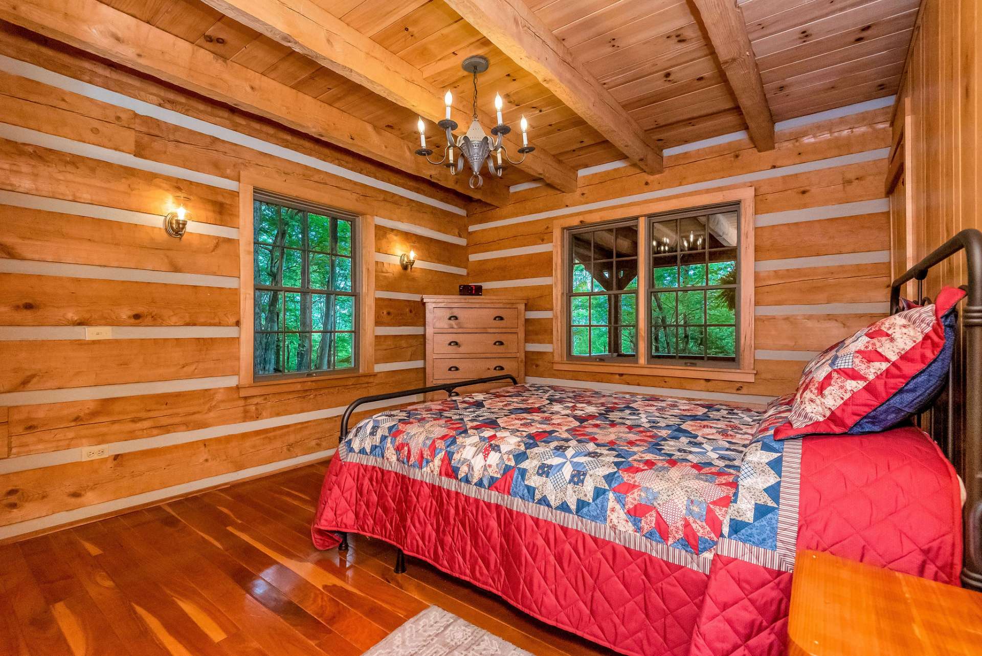 The primary bedroom, located on the main level, features log walls and exposed beams, adding to the rustic charm and cozy ambiance of the space.